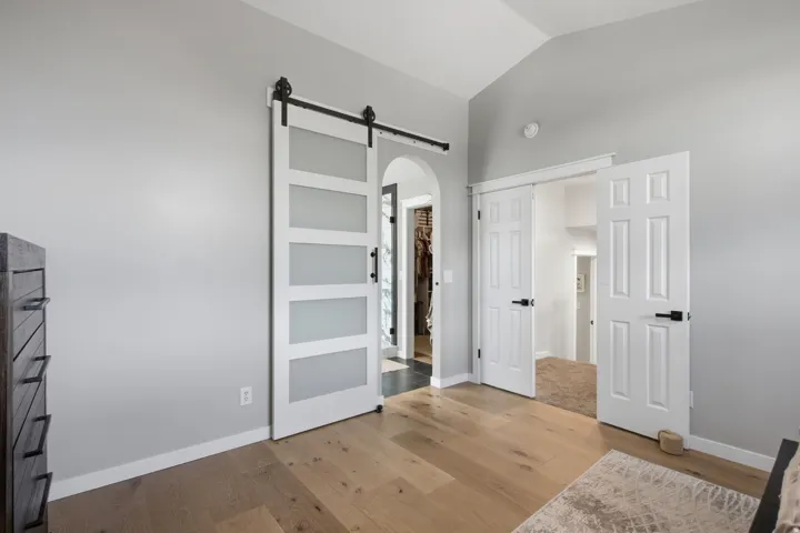 Vaulted ceiling, wood-finish flooring, modern barn door with frosted panels, white paneled interior doors, and arched entryway
