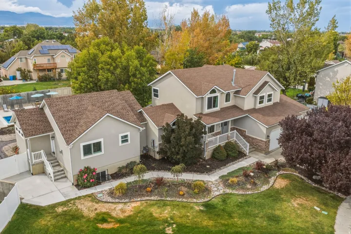 Multi-level residence featuring a stucco and stone veneer exterior, a prominent front porch with white railings, an attached garage, and mature landscaping with a manicured lawn