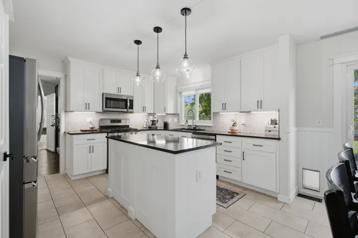 Kitchen featuring a central island, white shaker cabinetry, stainless steel appliances, and tile flooring
