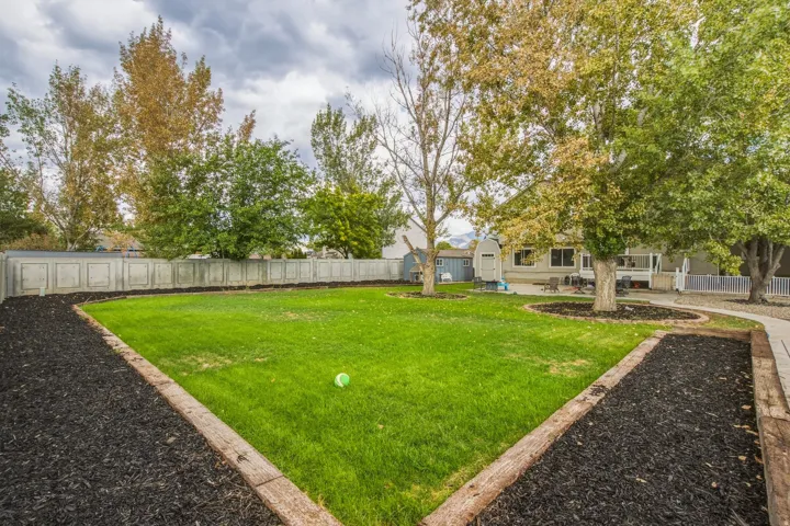 Expansive lawn area with mature trees, defined garden beds, and a perimeter fence