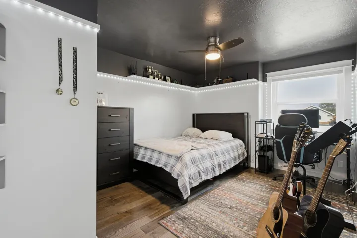 Wood-finish flooring, ceiling fan with integrated lighting, window with roller shade, and built-in shelving