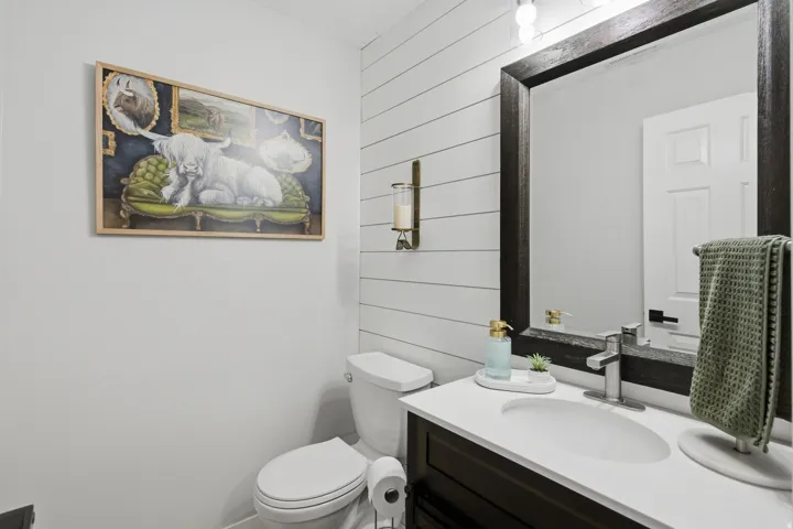 White shiplap accent wall, dark wood-framed mirror, vanity with white countertop, chrome faucet, and white paneled door