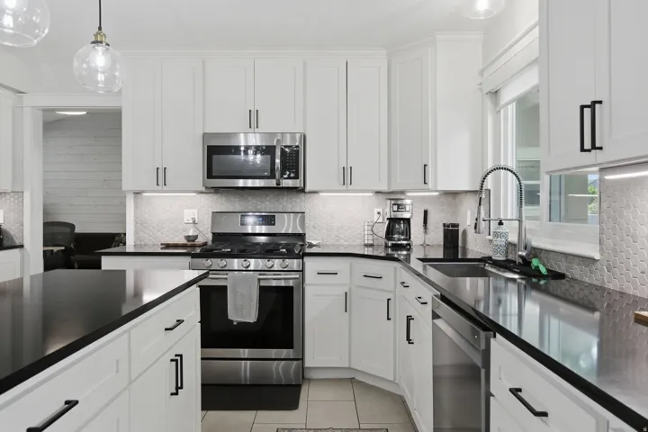 White cabinetry with matte black hardware, stainless steel appliances, black countertops, honeycomb tile backsplash, and an undermount sink