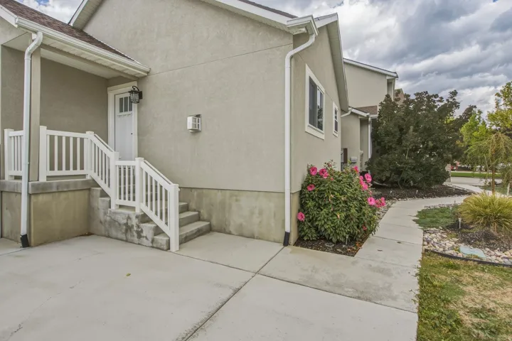 Stucco exterior featuring a covered porch, white railing, concrete steps, and a concrete pathway