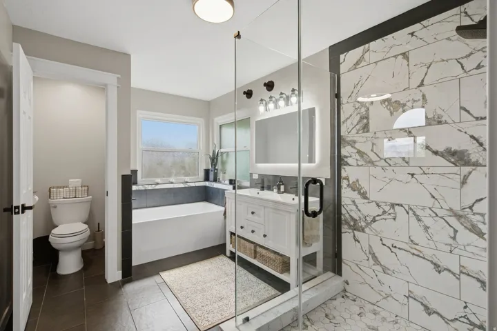 Glass-enclosed shower with large format marble-look tile and hexagonal floor tile