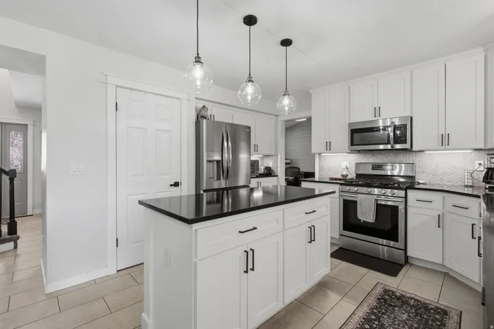 Gourmet kitchen featuring white cabinetry, stainless steel appliances, a center island with a dark countertop, pendant lighting, and tile flooring