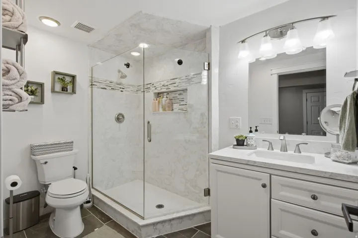 Enclosed glass shower with recessed lighting and a decorative tile accent band