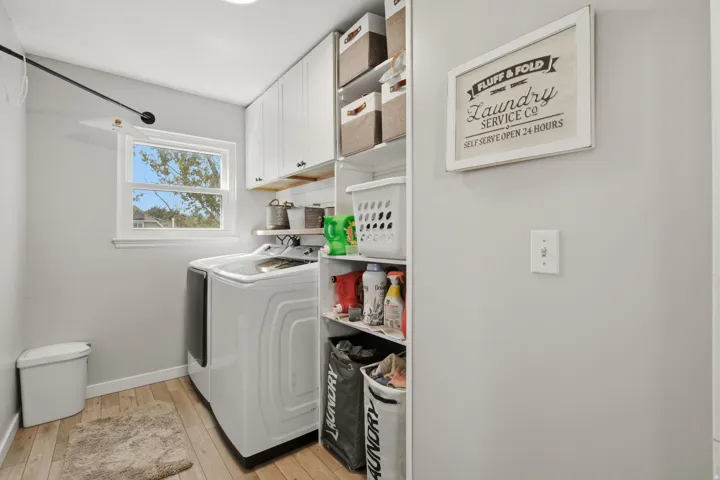 White shaker-style cabinetry with dark hardware, natural wood-finish flooring, built-in shelving, and a window with white trim