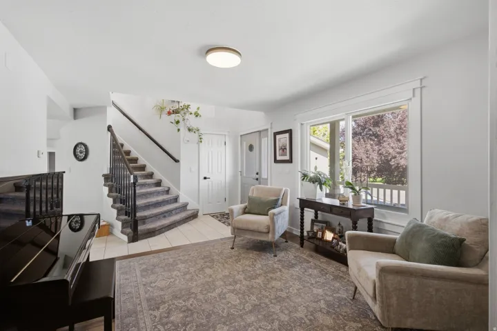 Carpeted staircase with dark wood handrail, tiled entryway, large window with trim detailing, and ceiling-mounted light fixture