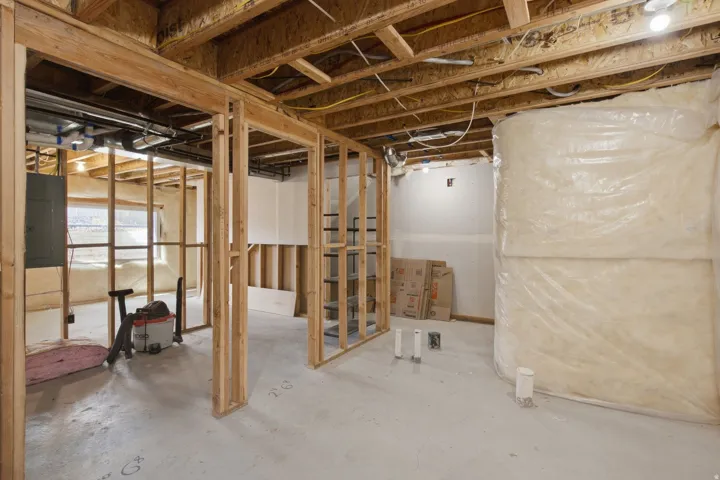 Unfinished basement space featuring visible wood framing, exposed ceiling joists, concrete flooring, and an electrical panel