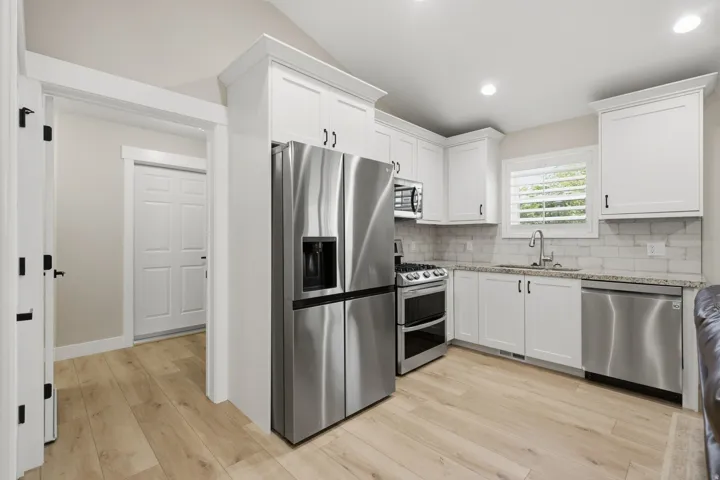 Kitchen featuring white cabinetry, stainless steel appliances, light-toned wood-finish flooring, and light granite countertops