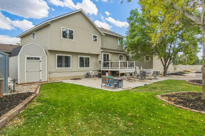 Spacious backyard featuring a multi-level deck, concrete patio, mature trees, and a storage shed