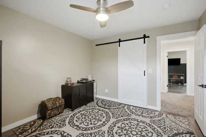 Ceiling fan with light fixture, wood-finish flooring, white trim, and a white barn door with black hardware