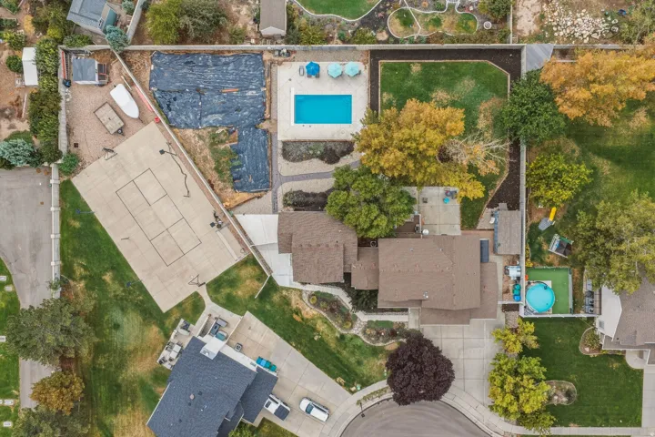 Expansive property featuring a swimming pool, concrete sport court, and a large residential structure with a brown shingle roof