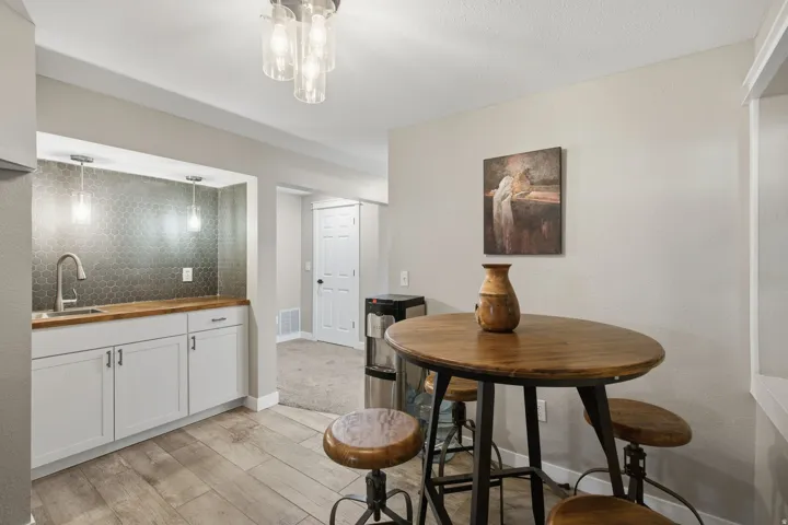Wet bar featuring a dark hexagonal tile backsplash, stainless steel sink, wood-finish countertop, and white cabinetry