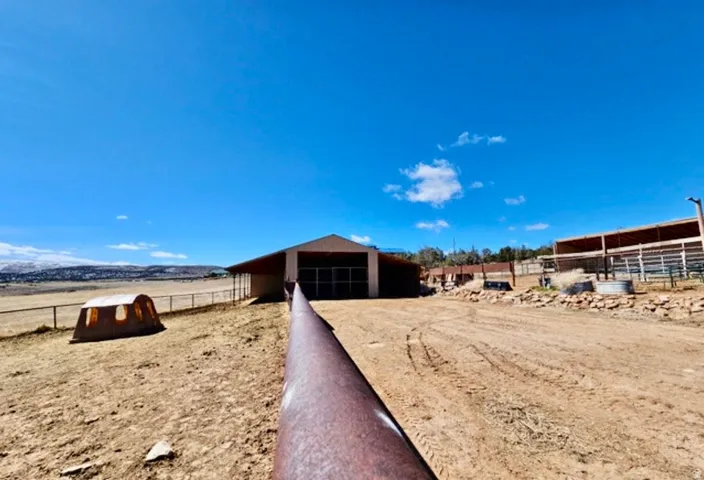 Expansive property featuring a large barn structure, fenced enclosures, and a wide open field