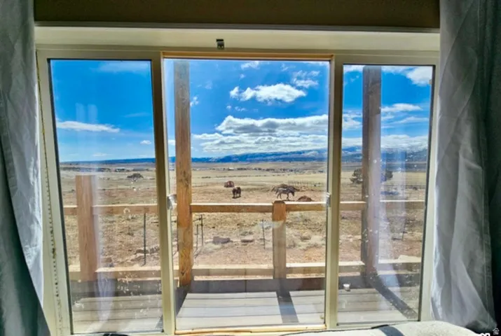 Sliding glass door opening to an outdoor deck with wood railings, overlooking expansive open terrain and distant mountains