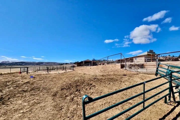 Extensive land area with perimeter fencing, a round pen, and distant mountainous terrain