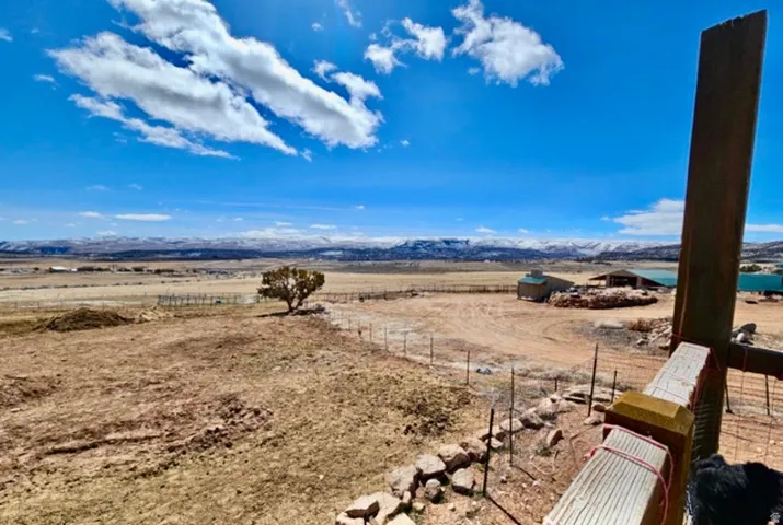 Expansive property with a distant mountain range backdrop, featuring a solitary tree and multiple outbuildings