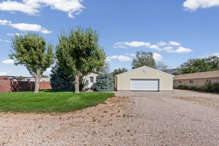 Detached garage with a white overhead door, gravel driveway, and a manicured lawn with mature trees