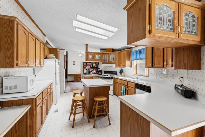 Wood-finish cabinetry with decorative glass inserts, white countertops, tile flooring, and a kitchen island with seating