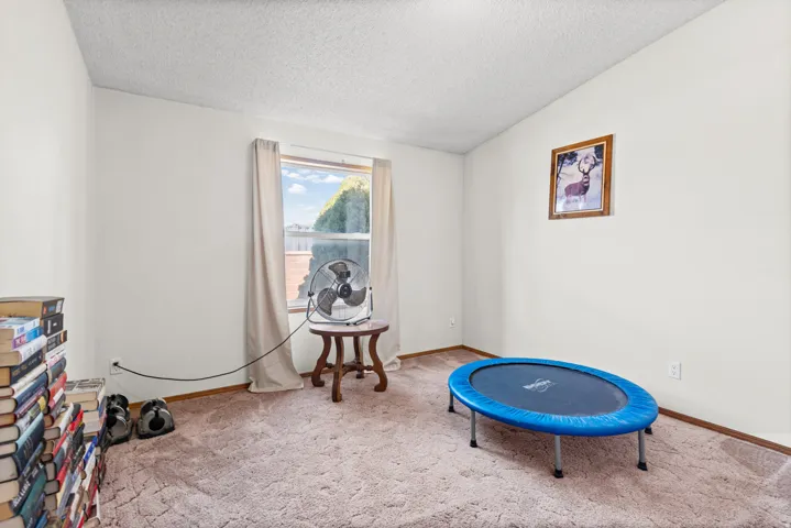 Carpeted room featuring a window with natural light, a wood-finish end table, and white painted walls