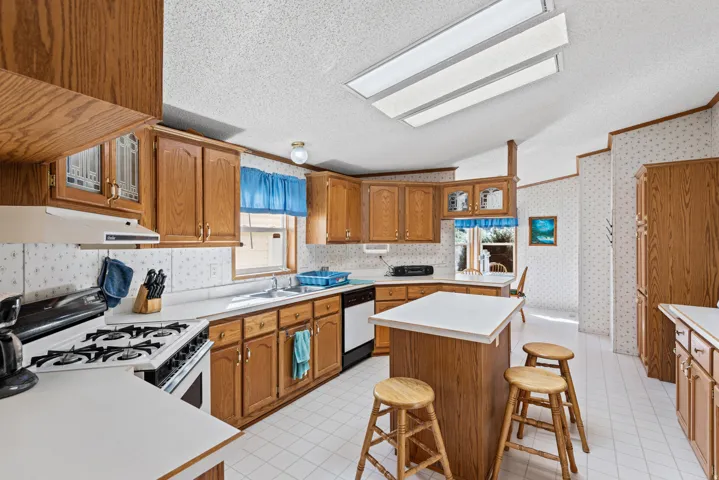 Kitchen featuring wood-finish cabinetry, white countertops, a central island, integrated dishwasher, and a white oven/range