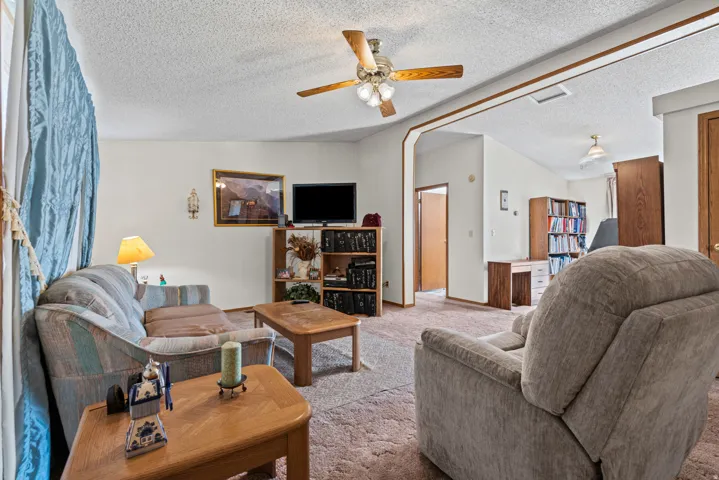 Recessed archway, ceiling fan with light fixture, textured ceilings, carpet flooring, and a wall-mounted light fixture