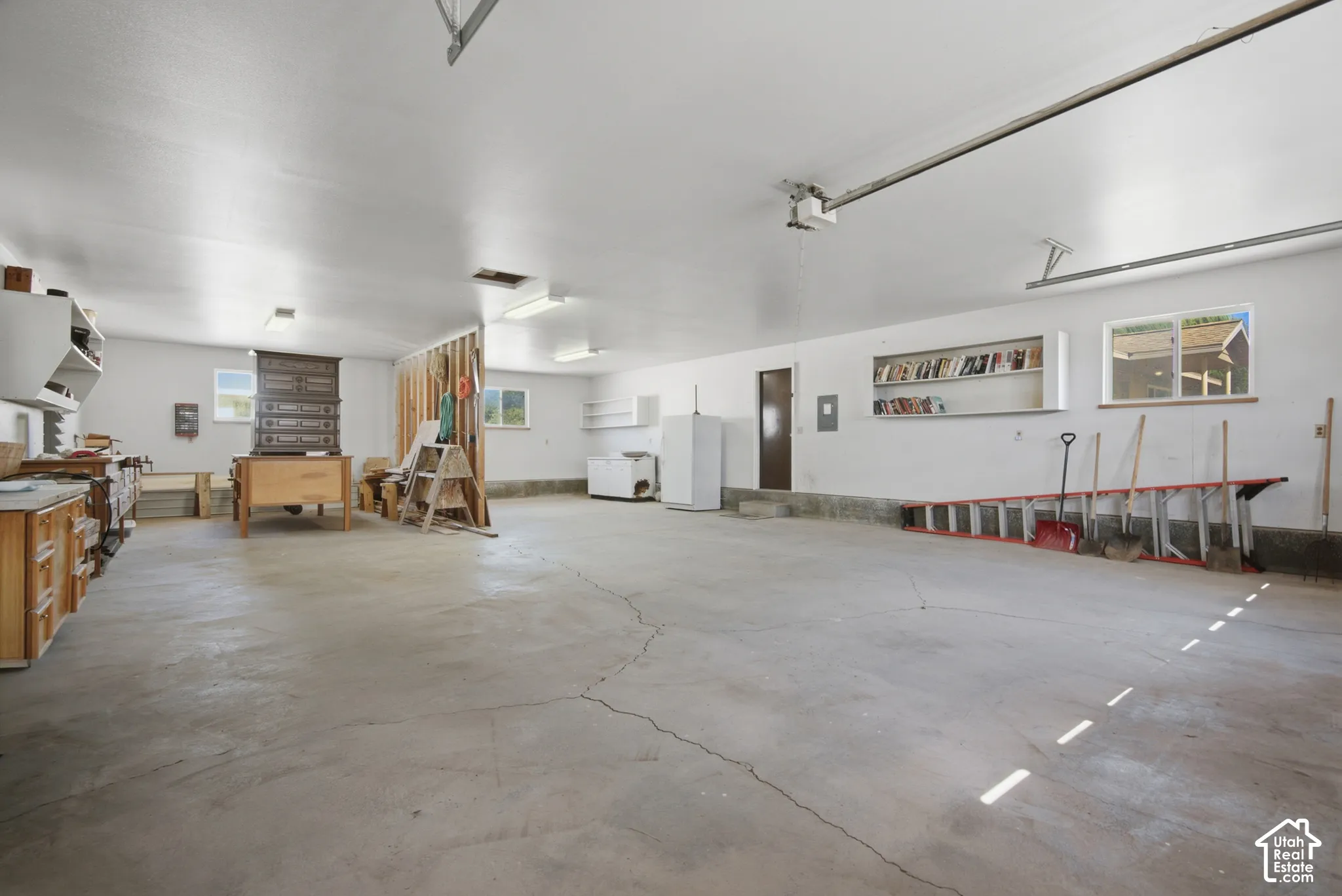 Spacious garage featuring a concrete floor, multiple windows, built-in shelving, and a workshop area with wood cabinetry