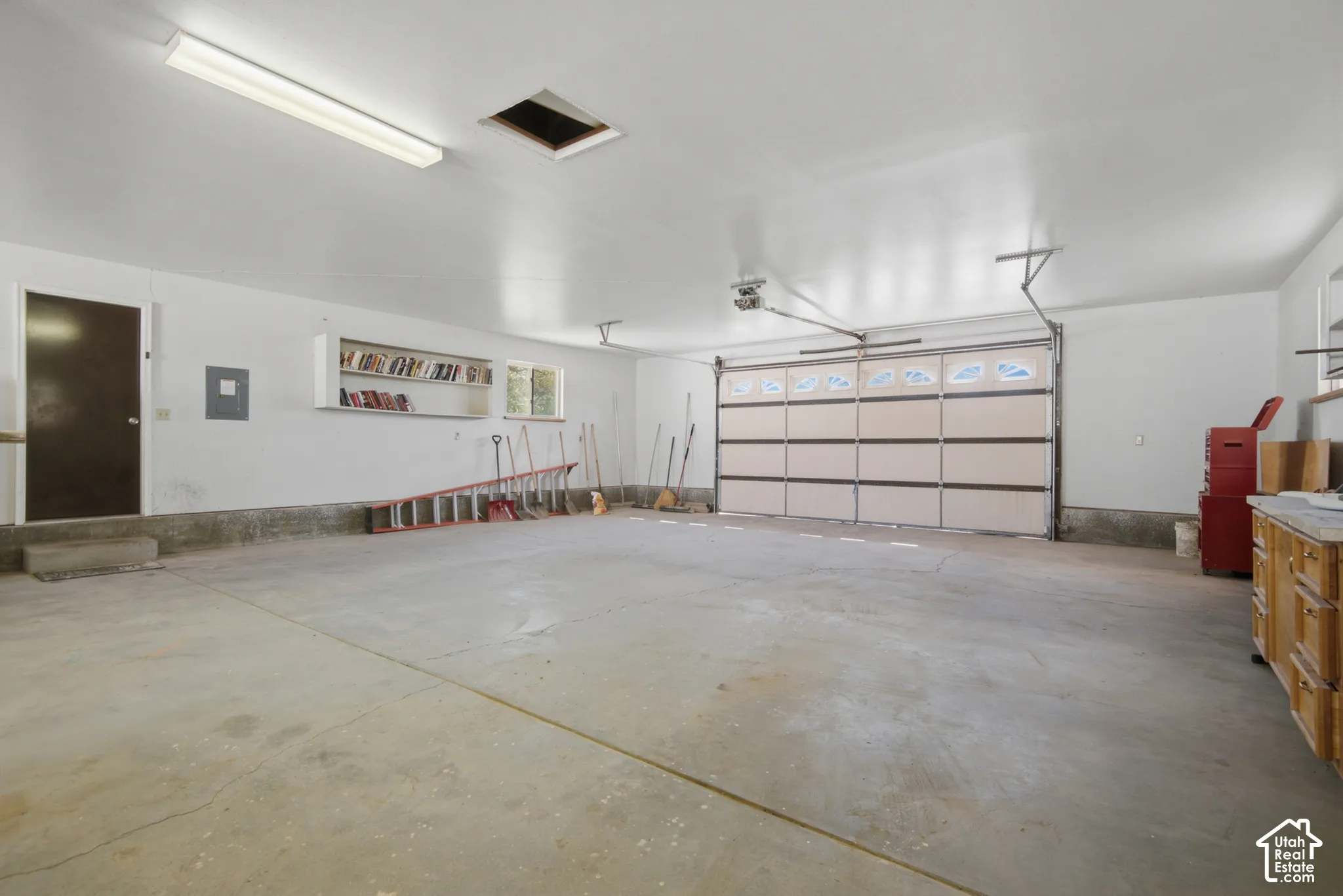 Spacious garage featuring a concrete floor, a built-in workbench with storage, an overhead garage door, and ample overhead lighting