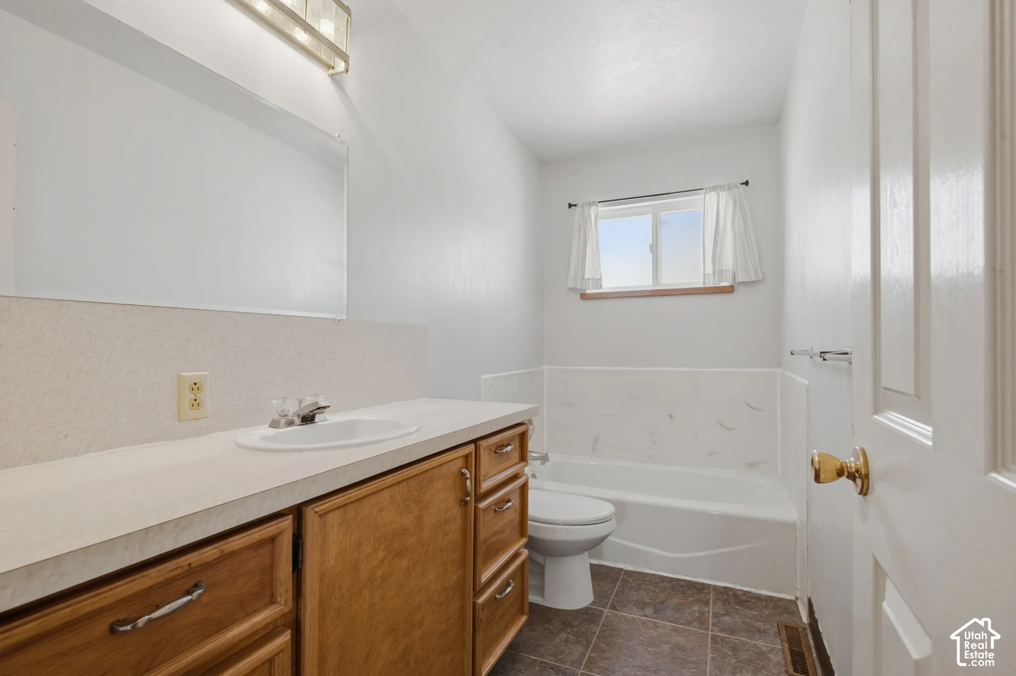 White vanity with wood-finish cabinetry, integrated sink, and an overhead vanity light