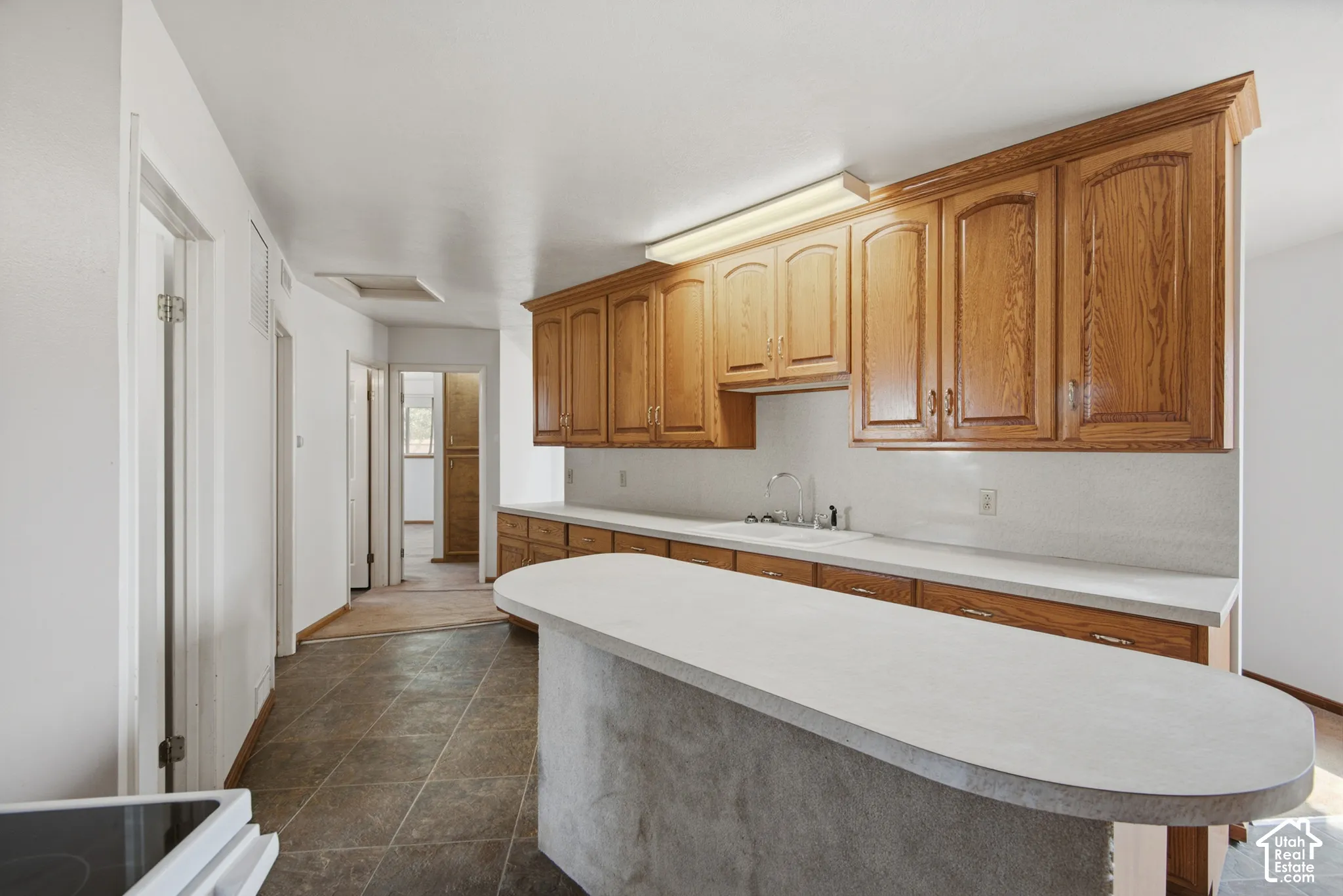 Kitchen featuring wood-finish cabinetry, solid surface countertops, a stainless steel sink, and tile flooring