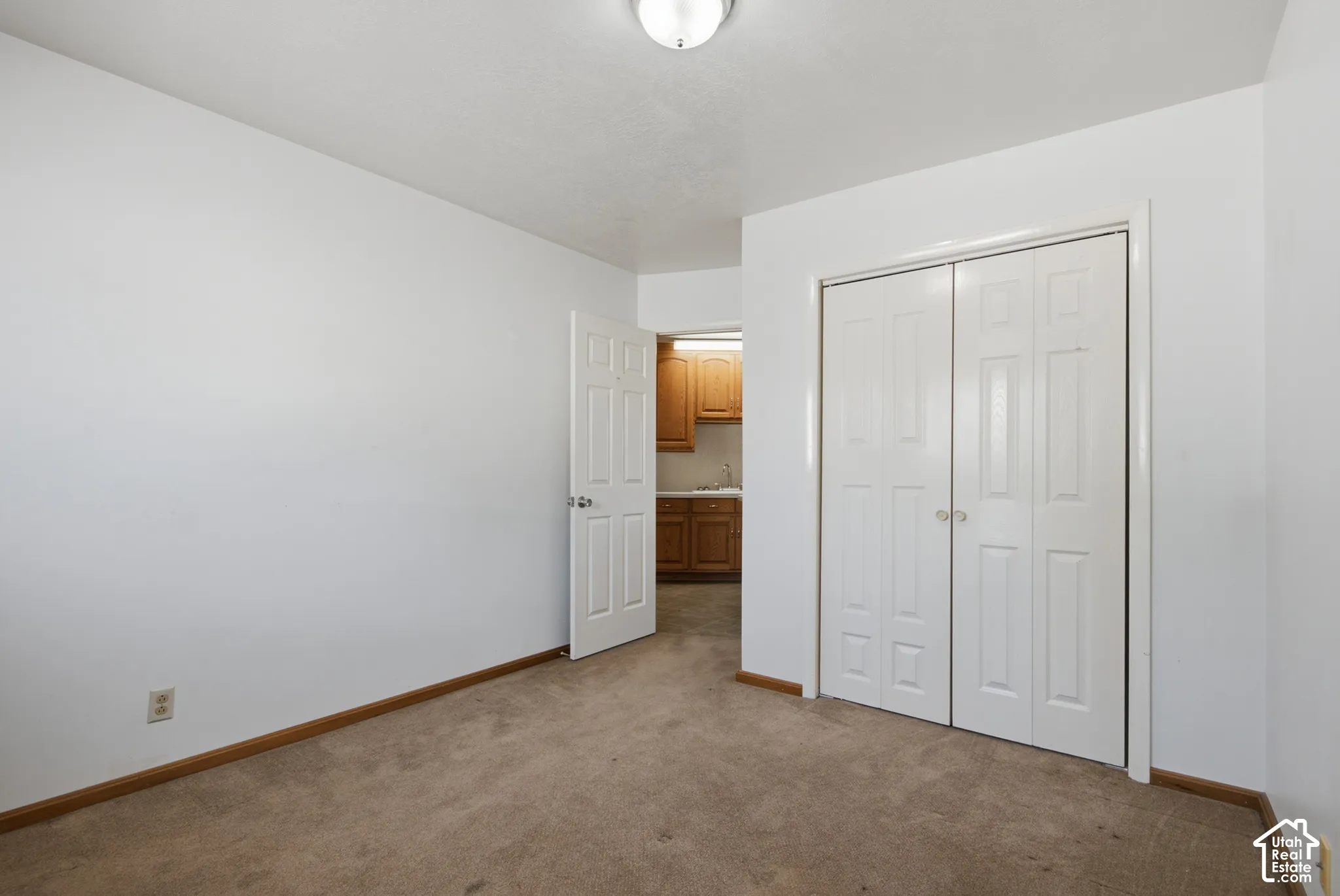 Carpeted room with a ceiling-mounted light fixture, white walls, and bi-fold closet doors