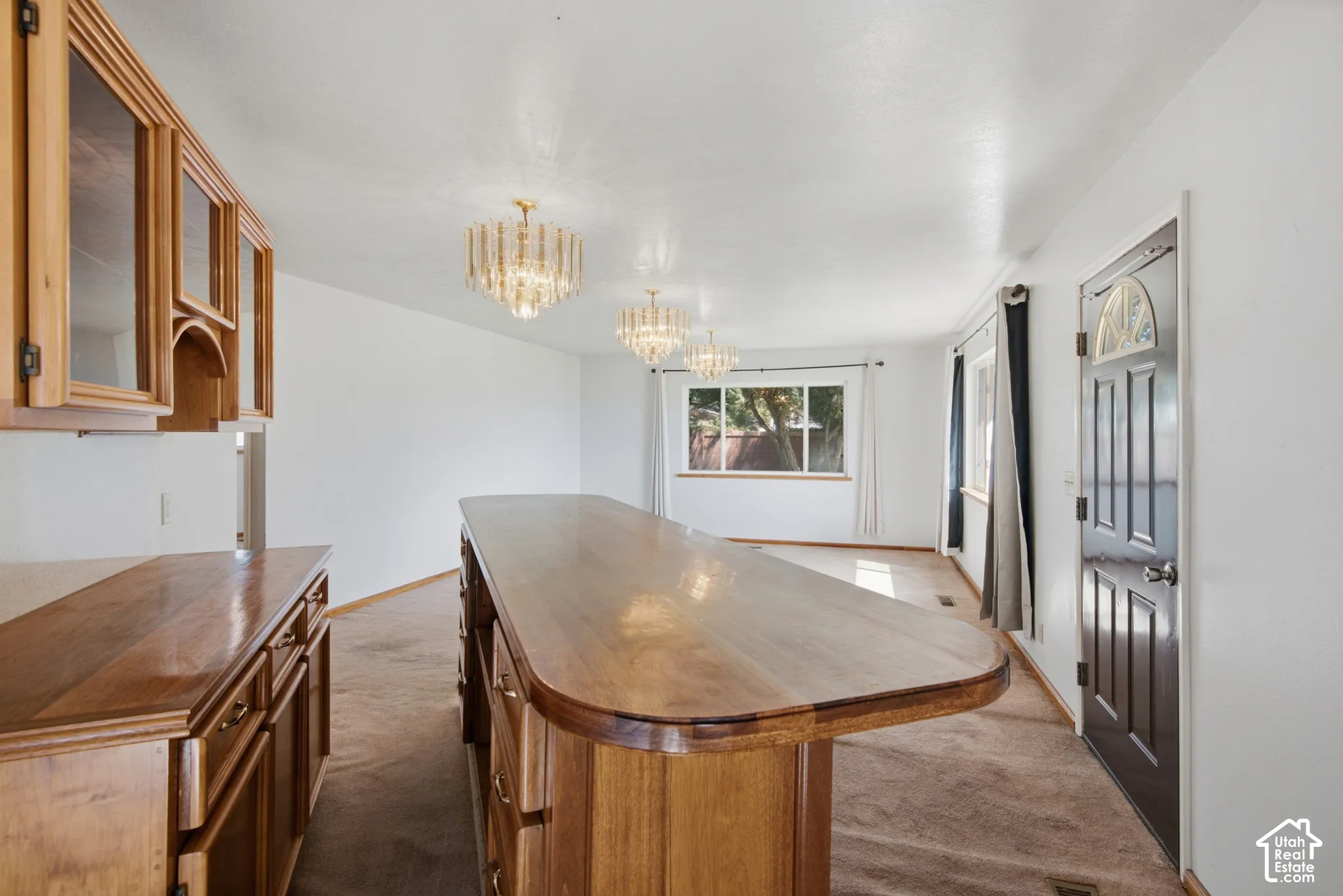 Wood-finish cabinetry and countertops, a spacious wood-finish island, and multiple crystal chandeliers illuminate the space