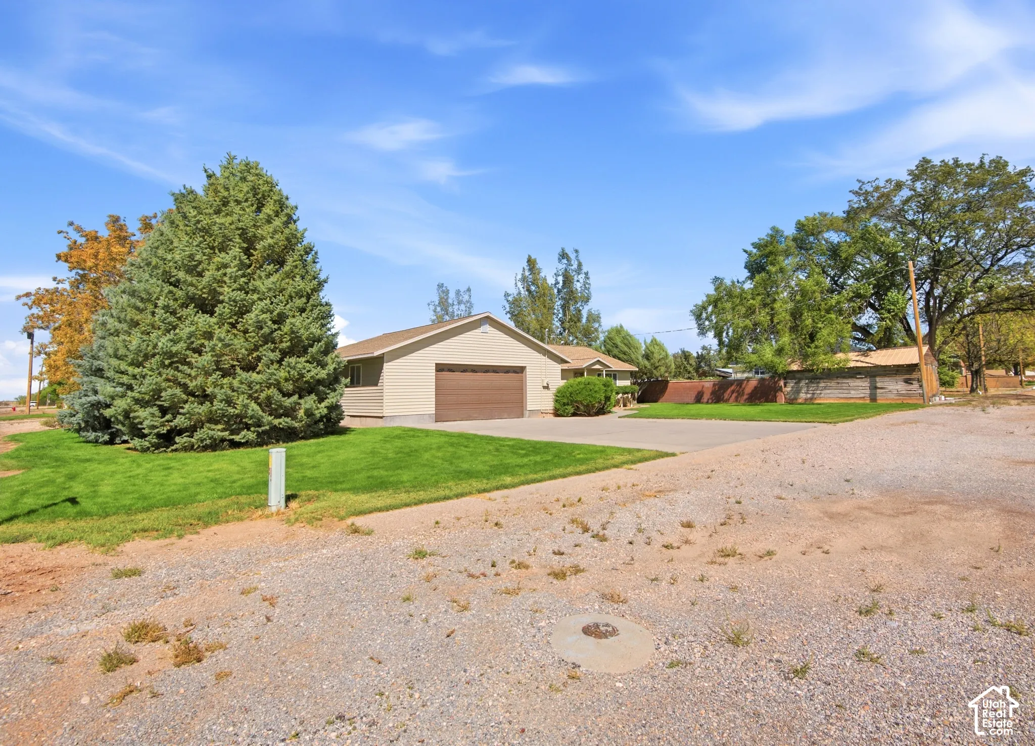 Single-story exterior featuring light-toned horizontal siding, a two-car garage, expansive manicured lawn, and mature evergreen trees