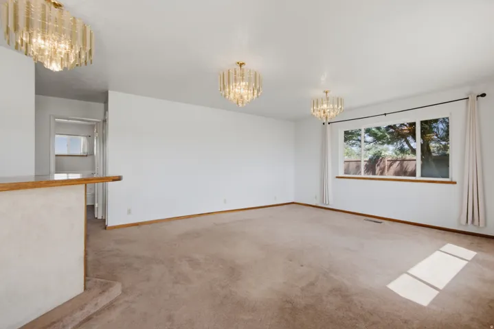 Wall-to-wall carpeting, three contemporary chandeliers, and a large window with wood trim