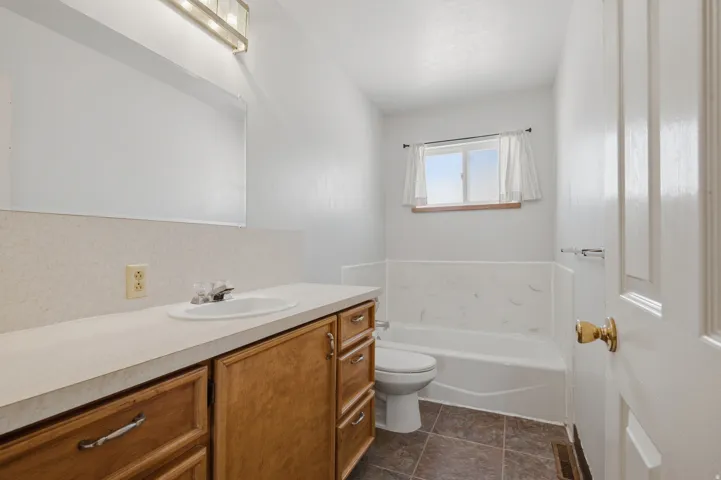 White vanity with wood-finish cabinetry, integrated sink, and an overhead vanity light