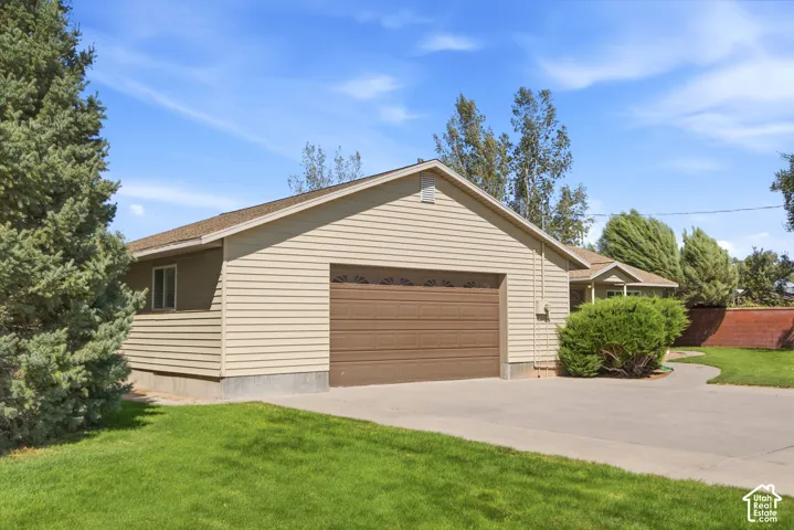 Detached two-car garage featuring beige horizontal siding, a concrete foundation, a concrete driveway, and mature landscaping