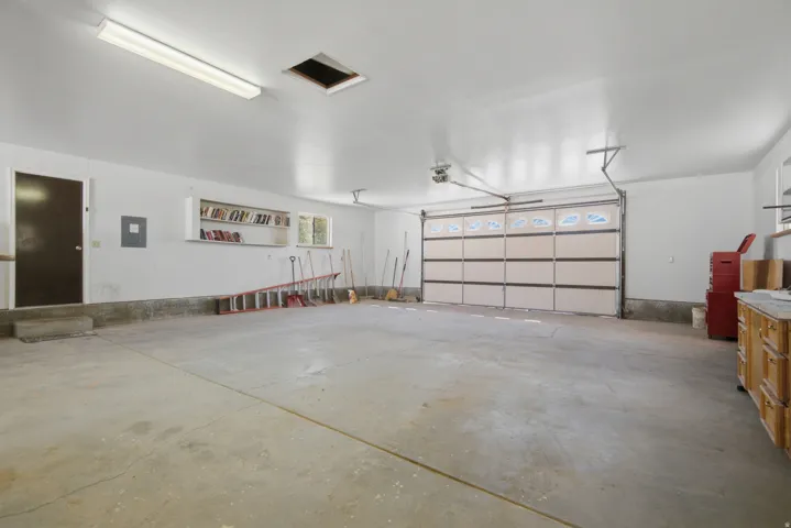 Spacious garage featuring a concrete floor, a built-in workbench with storage, an overhead garage door, and ample overhead lighting