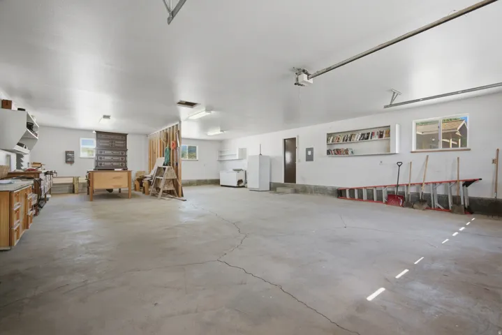 Spacious garage featuring a concrete floor, multiple windows, built-in shelving, and a workshop area with wood cabinetry