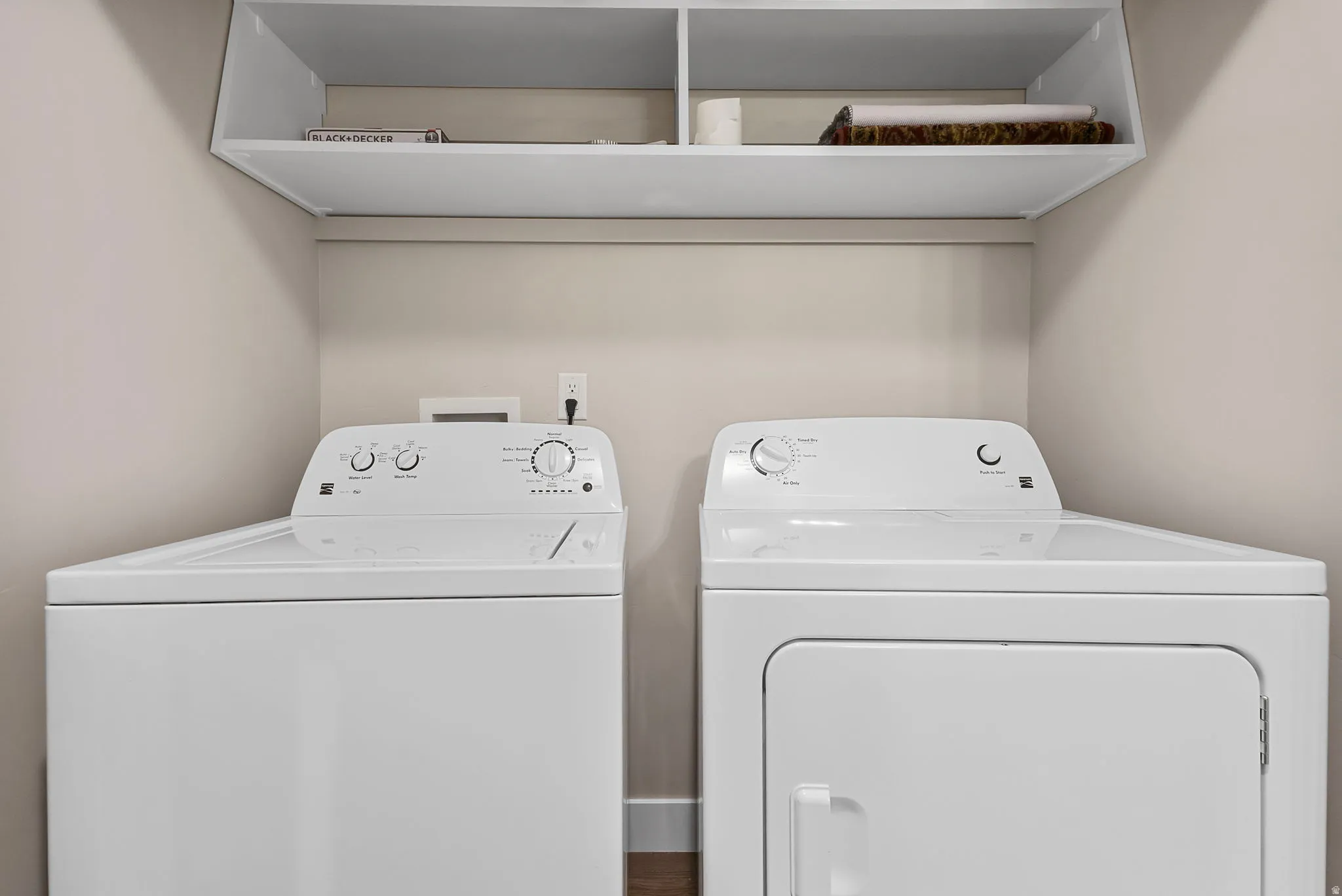 Laundry area with white top-load washing machine, white front-load dryer, and overhead built-in shelving