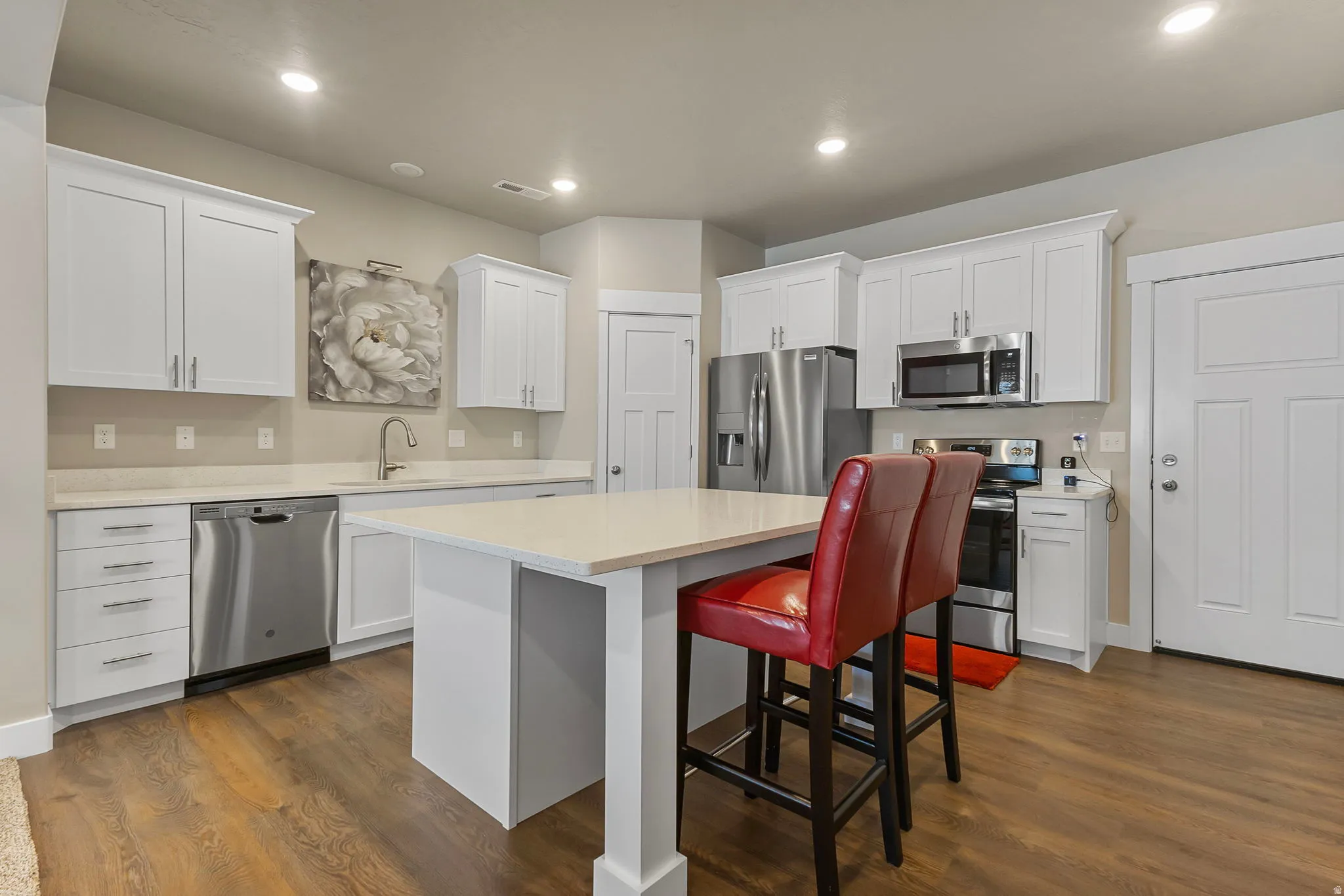 Kitchen featuring white cabinetry, stainless steel appliances, wood-finish flooring, recessed lighting, and a center island with countertop seating