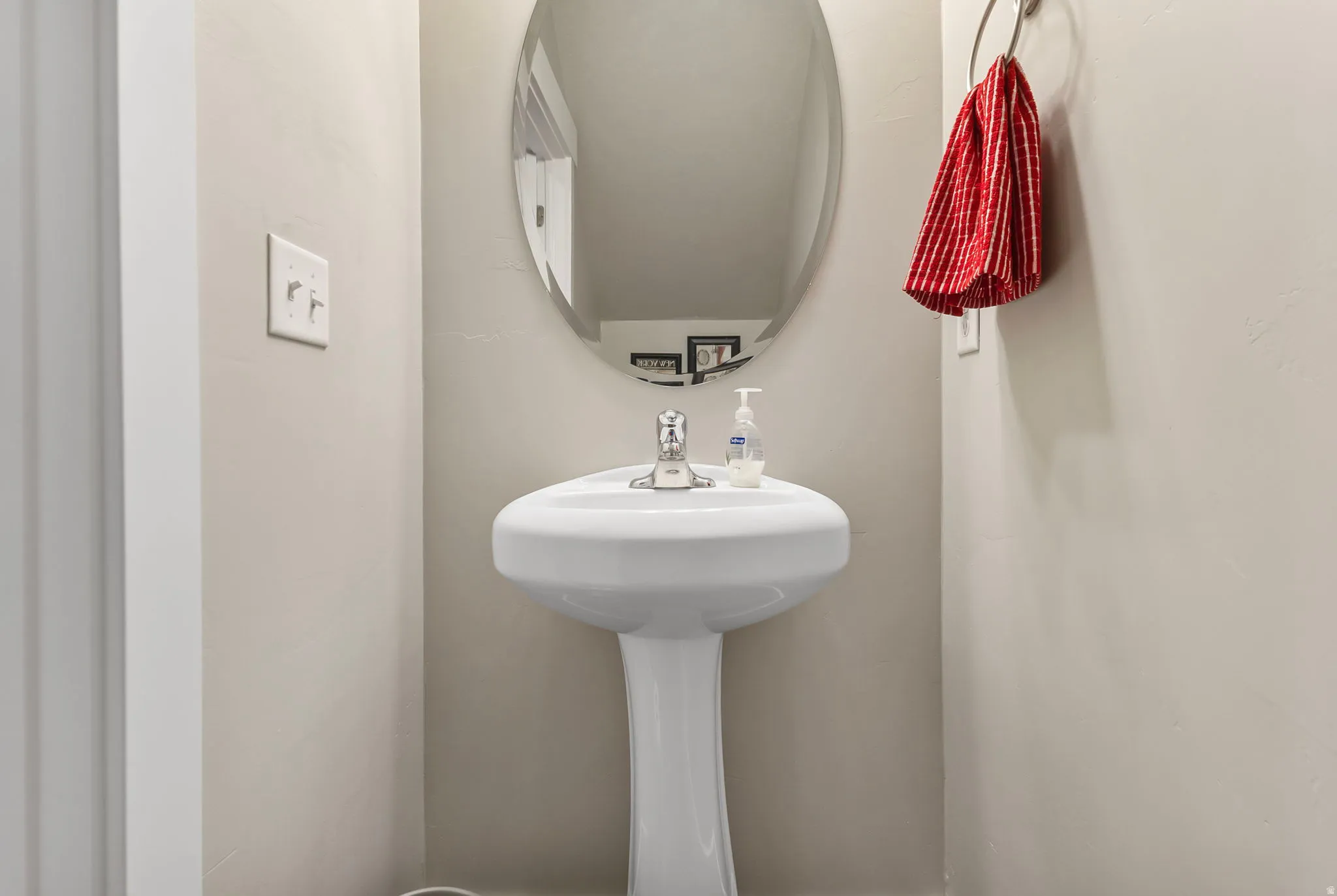 White ceramic pedestal sink with a chrome-finish faucet and an oval wall mirror