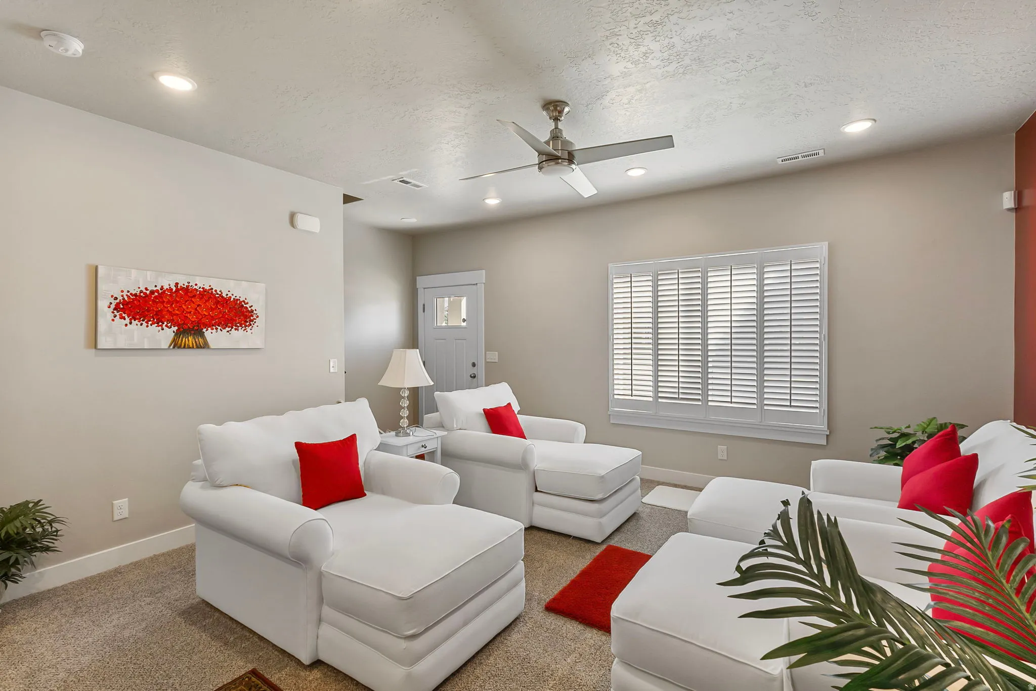 Recessed lighting throughout, ceiling fan, carpet flooring, window with white plantation shutters, and a white front door with decorative glass inserts