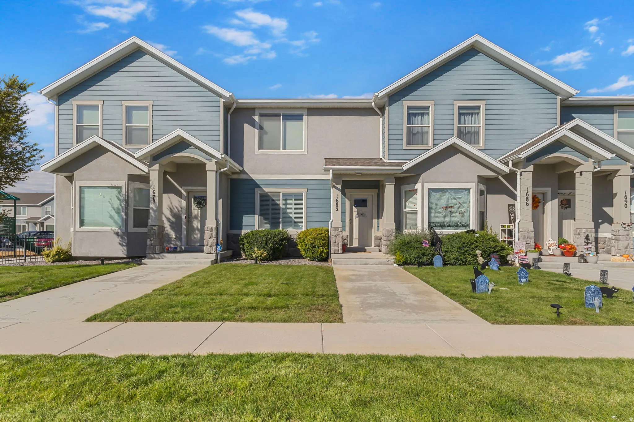 Two-story townhome with a light blue siding and gray stucco exterior, featuring a covered entry porch