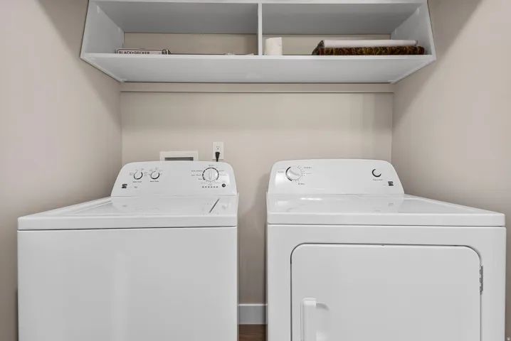 Laundry area with white top-load washing machine, white front-load dryer, and overhead built-in shelving