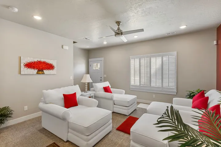 Recessed lighting throughout, ceiling fan, carpet flooring, window with white plantation shutters, and a white front door with decorative glass inserts