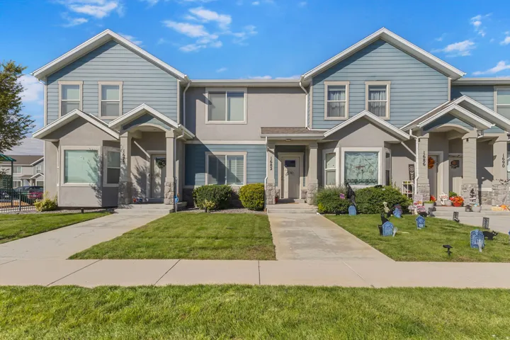 Two-story townhome with a light blue siding and gray stucco exterior, featuring a covered entry porch