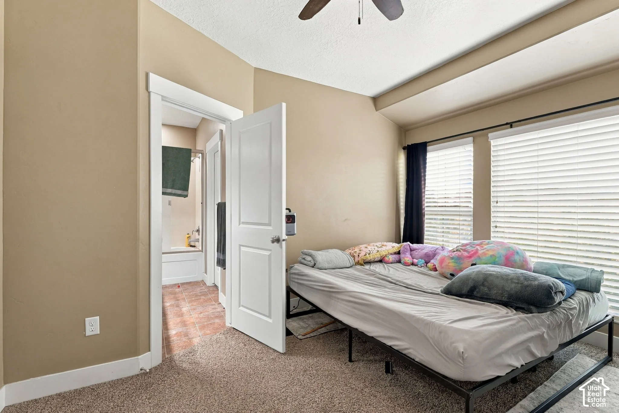 Carpet flooring with a ceiling fan, dual windows, and an en-suite bathroom featuring a shower-tub combination