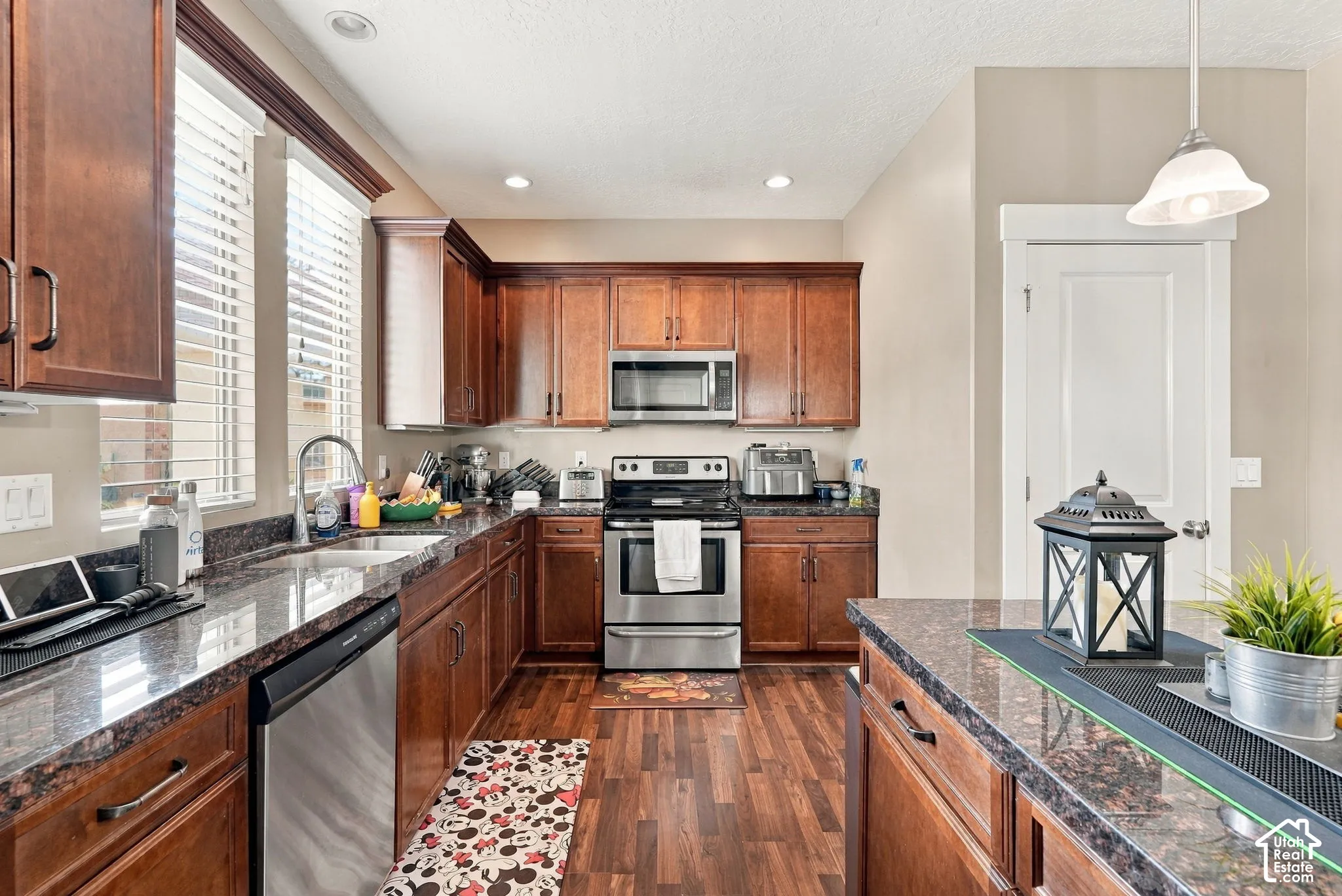 Kitchen featuring rich wood cabinetry, stainless steel appliances, dark granite countertops, and wood-finish flooring